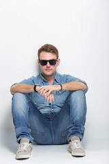Handsome caucasian man with a sunglasses on sitting on the floor
