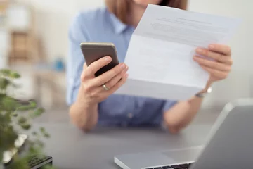 Fotobehang frau schaut auf einen brief und tippt auf ihr mobiltelefon © contrastwerkstatt