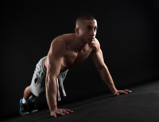 Obraz premium Young fitness man doing push-ups on floor, isolated on black background