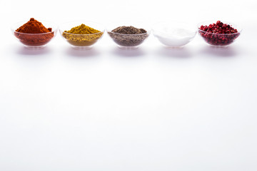 Paprika, Curry, Pfeffer, Salz und rote Pfefferkörner in Schalen und in Reihe arrangiert