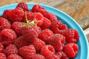 Red rasberry in blue green dish on old vintage wooden table.