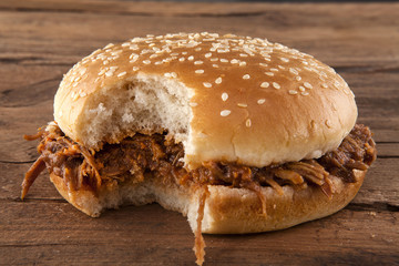 Pulled pork in a bun bitten on a side shot front on on wood