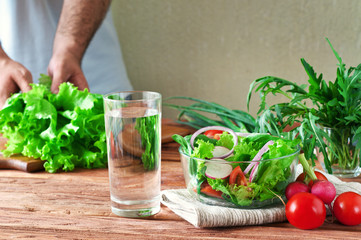 Vegetable salad in a bowl of glass. Arugula, lettuce, radishes, onions, cherry tomatoes. Against the background of the man hand holding a bundle of lettuce. Healthy lifestyle concept. copy space