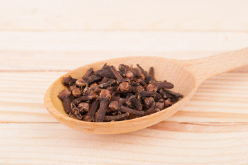 Cloves in spoon close up on a wooden table.