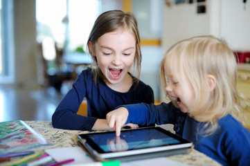 Two little sisters playing with a digital tablet