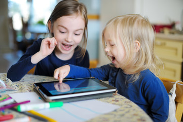 Fototapeta premium Two little sisters playing with a digital tablet