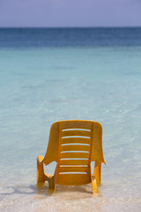 One orange plastic chair standing in the water on tropical beach
