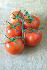 Red ripe tomatoes on green branch lying on wooden background closeup