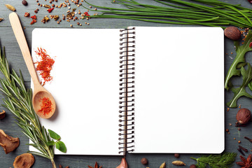 Open recipe book with fresh herbs and spices on wooden background