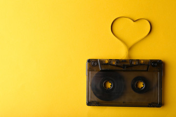 Audio cassette with magnetic tape in shape of heart on yellow background