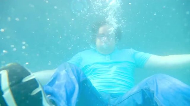 Man sits on the bottom of a pool in full clothing