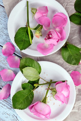 Beautiful pink roses in white plates on wooden table with parchment, top view