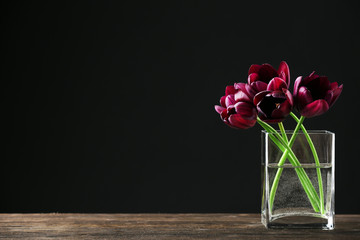 Beautiful purple tulips in glass vase on black background