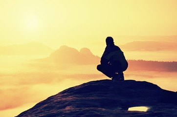 Rear view of male hiker sitting on the rocky peak  while enjoying a colorful daybreak above mounrains valley