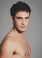 Beautiful (handsome) muscular male model with nice body posing over light-gray background.