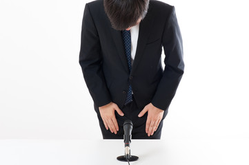記者会見でマイクを使って謝罪している役員