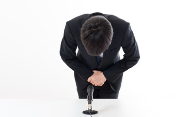 記者会見でマイクを使って謝罪している役員