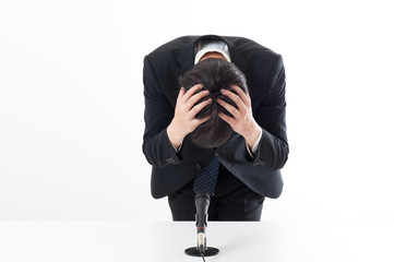 記者会見でマイクを使って謝罪している役員