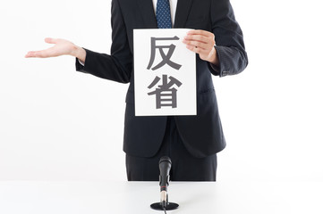 記者会見でマイクを使って謝罪している役員
