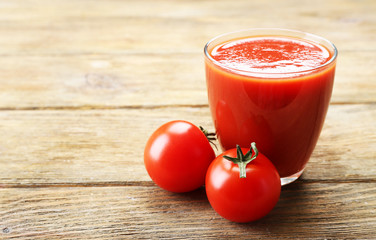 Glass of fresh tomato juice on wooden background