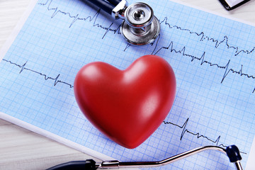 Cardiogram with stethoscope and red heart on table, closeup