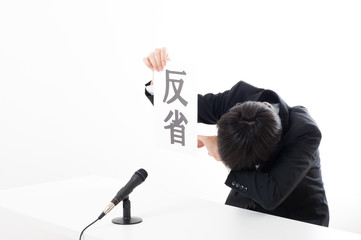 記者会見でマイクを使って謝罪している役員
