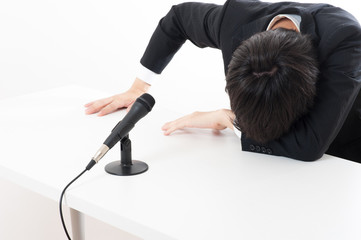 記者会見でマイクを使って謝罪している役員