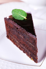 Piece of chocolate cake with mint on white plate, closeup