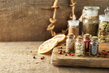 Assortment of spices in glass bottles on cutting board, on wooden background