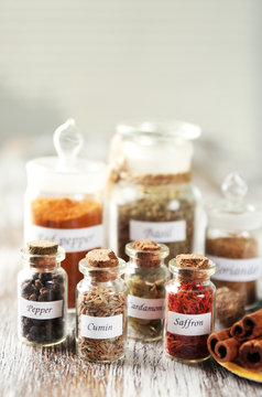 Assortment of spices in glass bottles on wooden table, on light background