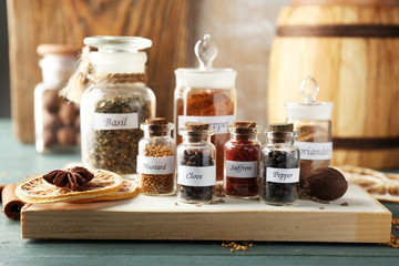 Assortment of spices in glass bottles on cutting board, on wooden background