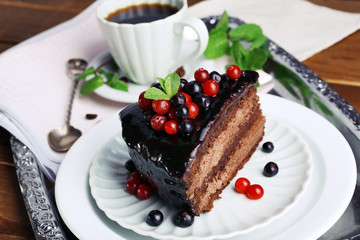 Delicious chocolate cake with berries and cup of coffee on table close up