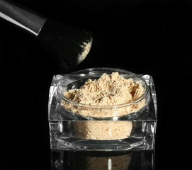 Jar with loose cosmetic powder and makeup brush, isolated on black