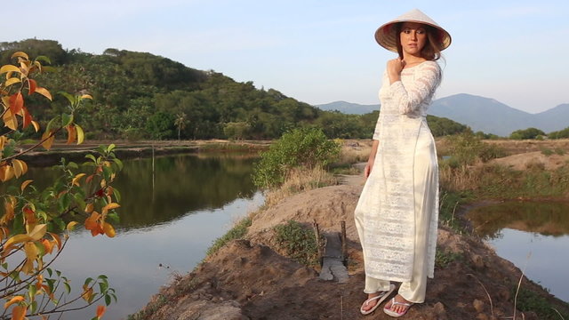 blonde girl in vietnamese costume and hat poses between ponds 
