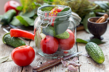 Vegetables and herbs in the glass jar on a wooden table.