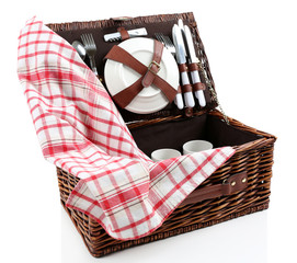 Wicker picnic basket with tableware and tablecloth isolated on white