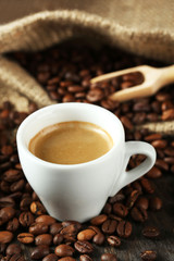 Cup of coffee with beans on table close up