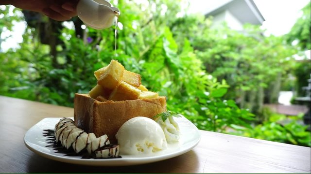 Human hand poring syrub in to Honey toast with vanilla ice cream and banaba with nature background