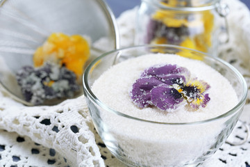 Candied sugared violet flowers, in glass jar and bowl, on wooden background