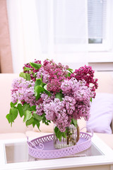 Beautiful lilac flowers in vase on table of interior background