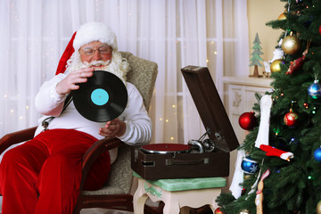 Santa Claus sitting in comfortable chair near retro turntable at home