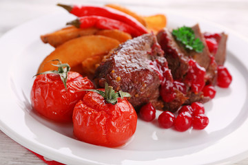 Tasty roasted meat with cranberry sauce and roasted vegetables on plate, on color wooden background