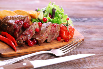 Beef with cranberry sauce, roasted potato slices on cutting board, on wooden background