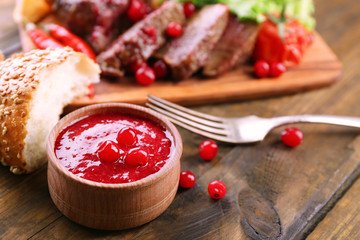 Beef with cranberry sauce, roasted potato slices on cutting board, on wooden background