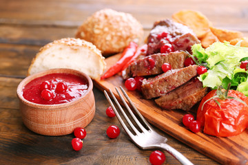 Beef with cranberry sauce, roasted potato slices on cutting board, on wooden background