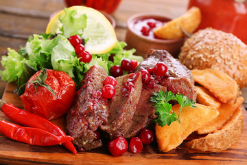 Beef with cranberry sauce, roasted potato slices on cutting board, on wooden background