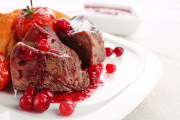 Tasty roasted meat with cranberry sauce and roasted vegetables on plate, on light background