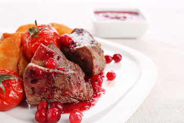 Tasty roasted meat with cranberry sauce and roasted vegetables on plate, on light background