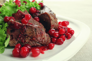 Tasty roasted meat with cranberry sauce on plate, on light background