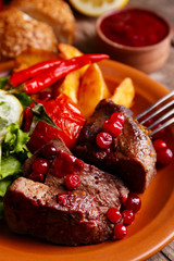 Tasty roasted meat with cranberry sauce, salad and roasted vegetables on plate, on wooden background